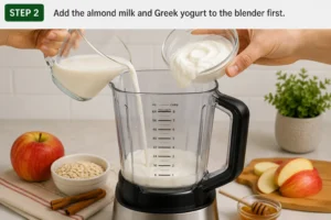Pouring almond milk and Greek yogurt into a blender for the Apple Cinnamon Smoothie recipe.