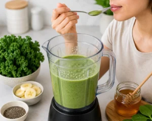 Tasting a homemade kale smoothie with a spoon and adjusting the sweetness with honey before serving.